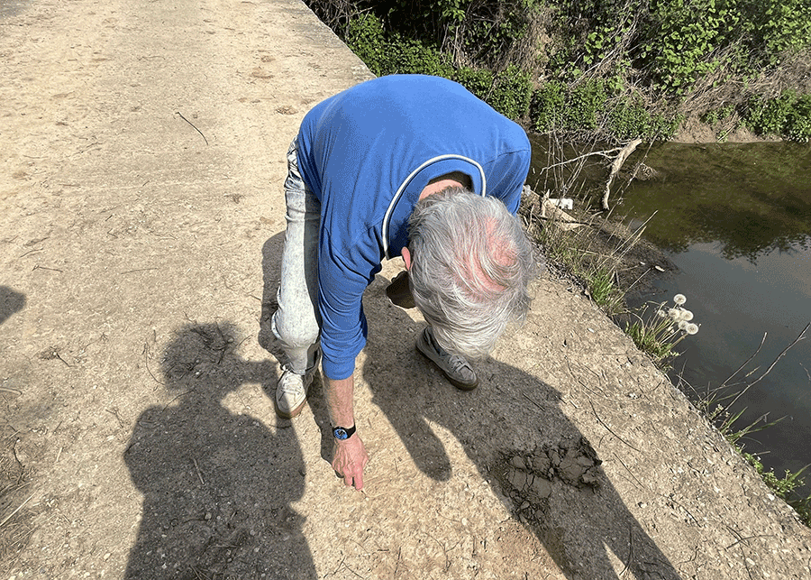 Man tracing the course of irrigation ditches in the dust beside a water channel.